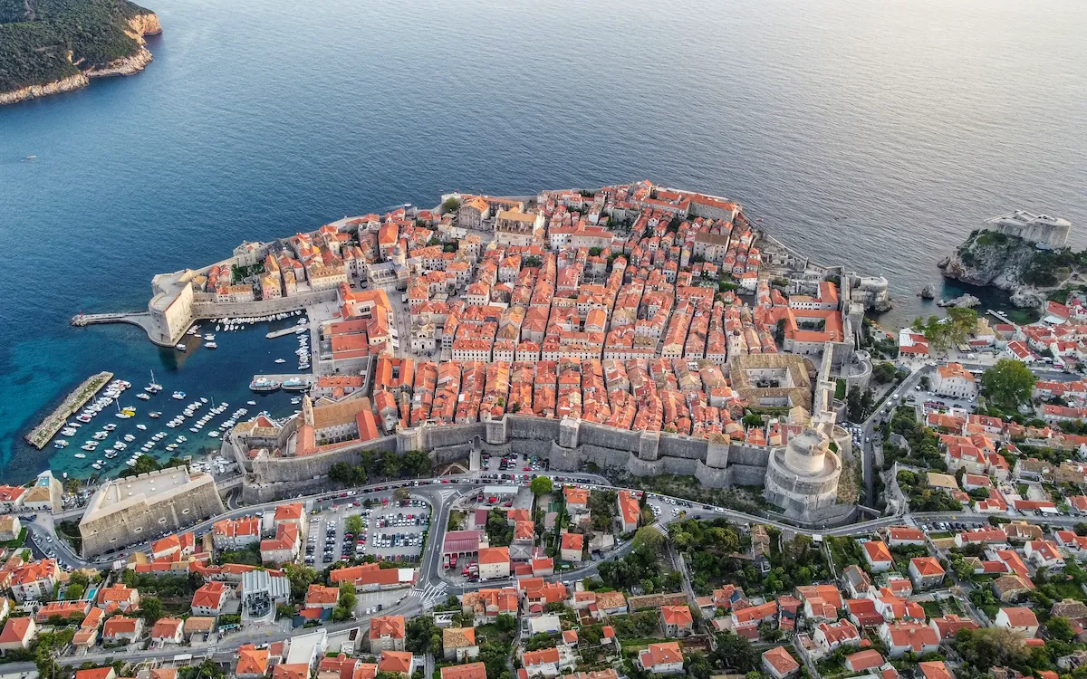 A classic top-down view from near the top cable car station, showcasing the full outline of Dubrovnik Old Town, its historic harbor, fortresses, and terracotta rooftops