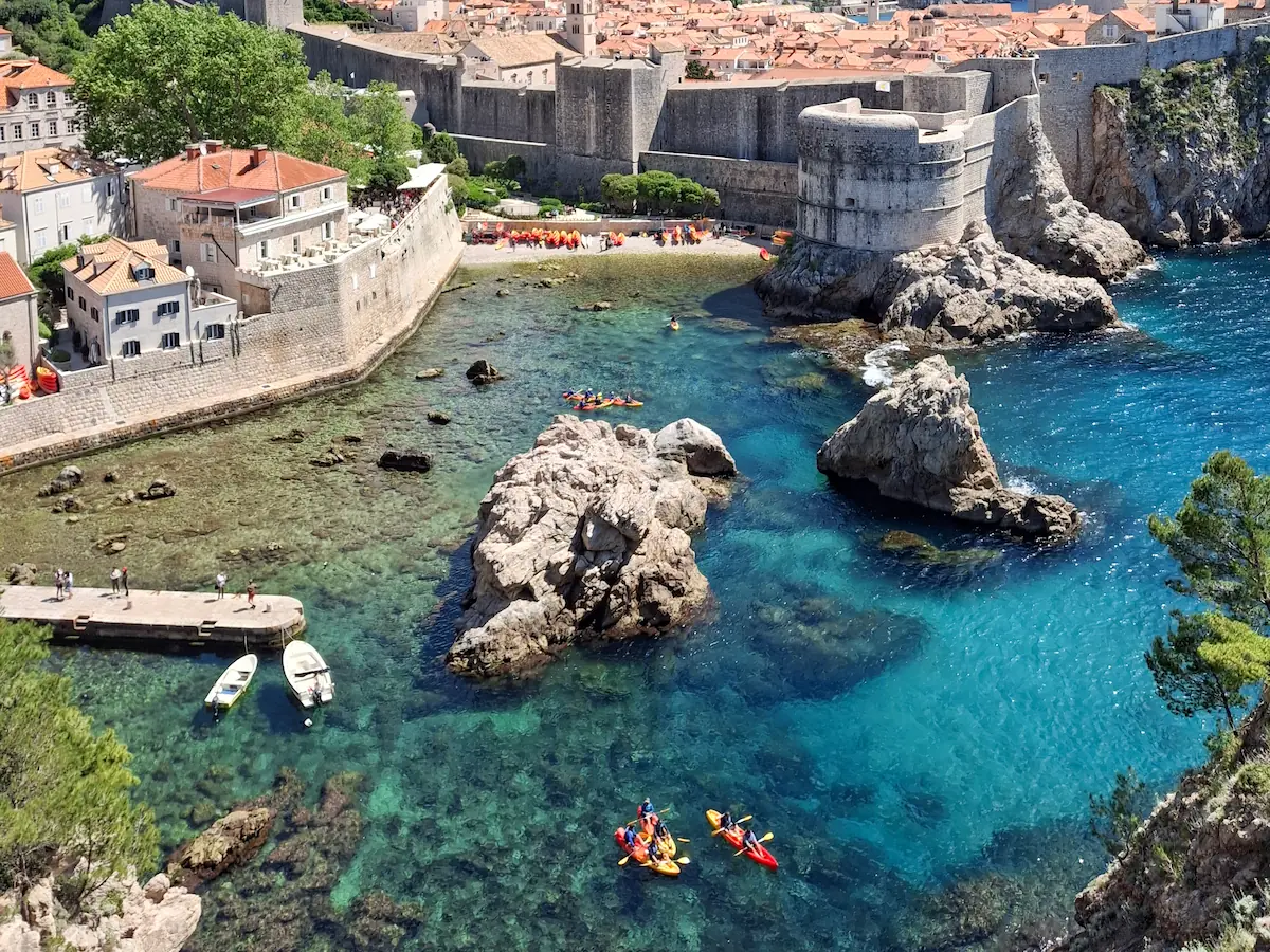 High angle view from Fort Lovrijenac looking down at kayaks launching into the clear turquoise water of Pile Bay