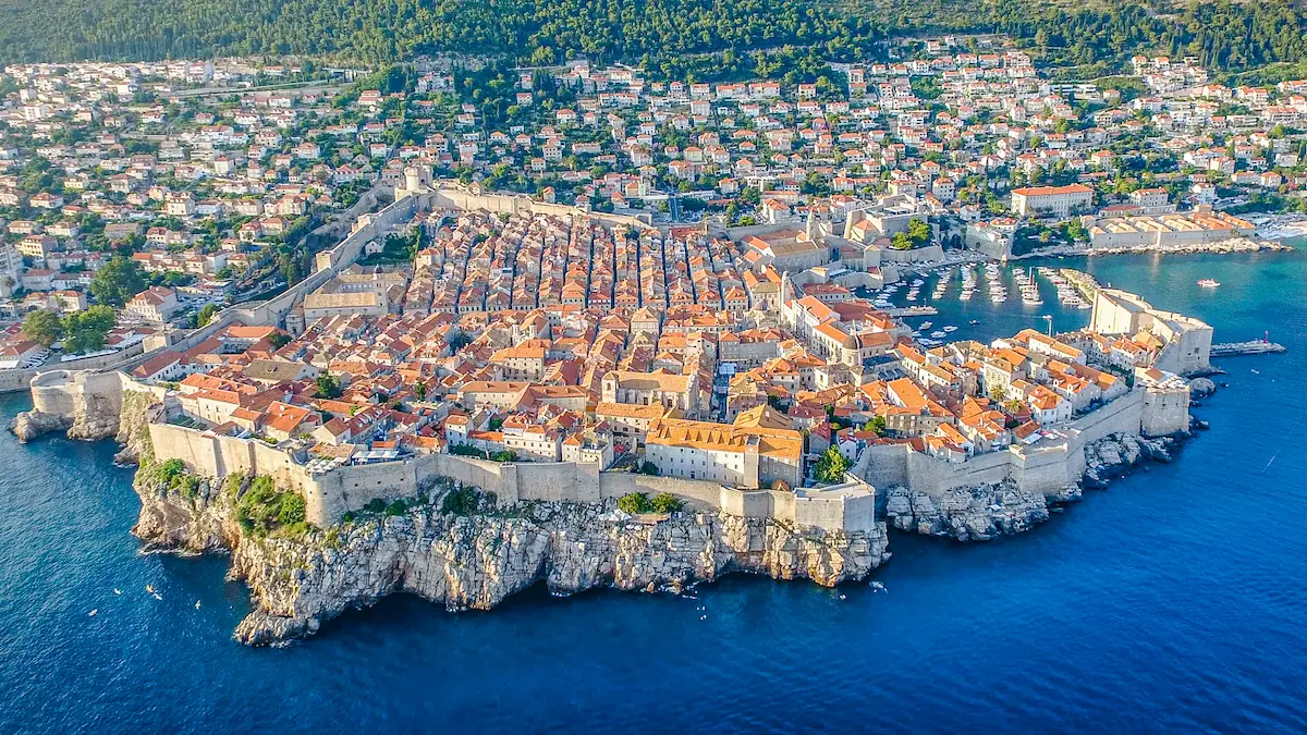 Aerial view of Dubrovnik City Walls surrounding the Old Town, showing stone fortifications, towers, bastions, terracotta rooftops, and the Adriatic coastline