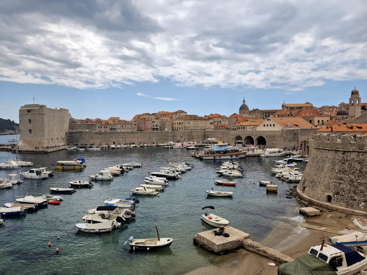 View from the wooden Revelin drawbridge next to Ploče Gate, looking down over the historic Old Town harbor and Lokrum Island across the blue water