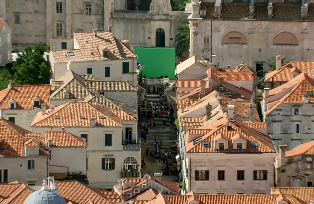 High-angle production still of a Game of Thrones filming location in Dubrovnik, featuring a massive green screen at the top of the Jesuit Staircase surrounded by historic stone buildings and orange terracotta roofs
